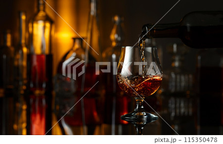 Pouring brandy from a bottle into a glass. Pouring brandy from a bottle into a glass. 115350478
