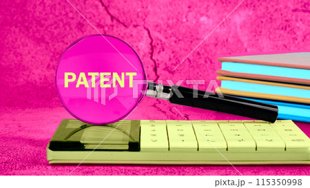 Copyright concept. PATENT writing through a magnifying glass on a calculator on a bright background with a stack of business notebooks in the background Copyright concept. PATENT writing through a magnifying glass on a calculator on a bright background with a stack of business notebooks in the background 115350998