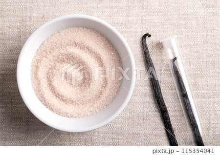 Vanilla sugar, flavored sugar in a white bowl on linen fabric, next to dried, brown, ripe pods or beans of Vanilla planifolia, a spice with distinctive flavor, used for baking and food flavoring. 115354041