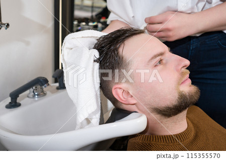 A hairdresser wipes client man head with a white towel after washing in a barbershop. 115355570