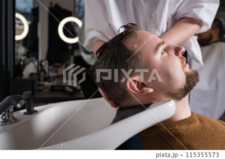 Barber shampooing washing a male clients head in the sink. Barber shampooing washing a male clients head in the sink. 115355573