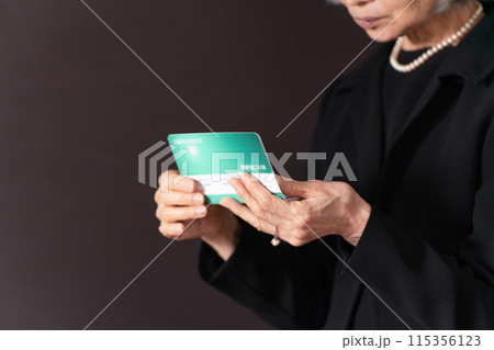 通帳を見て嘆く喪服のシニア女性　手元 115356123