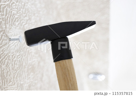 hammer drives nail into white wall at home 115357815