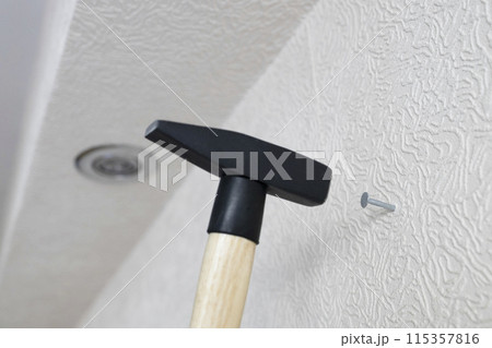 hammer hammers nail into white wall hammer hammers nail into white wall 115357816