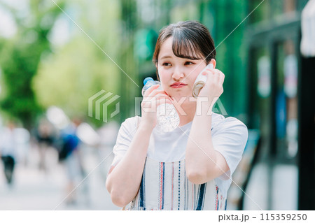 猛暑に耐えペットボトルで体を冷やす若い女性 115359250