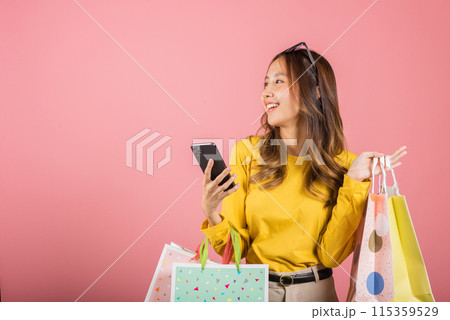 Portrait Asian happy beautiful young woman teen shopper smiling standing excited holding online shopping bags online colorful on mobile phone or smartphone studio shot isolated on pink background 115359529