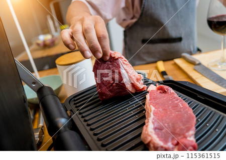 Chef at the kitchen preparing beef steaks on the home electric grill 115361515