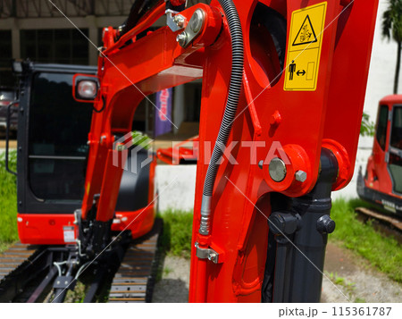 Red large excavators are stationed in a green field in front of a building 115361787