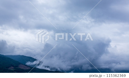 雨の日の山頂を、覆いかぶさりながら流れていく雨雲 115362369