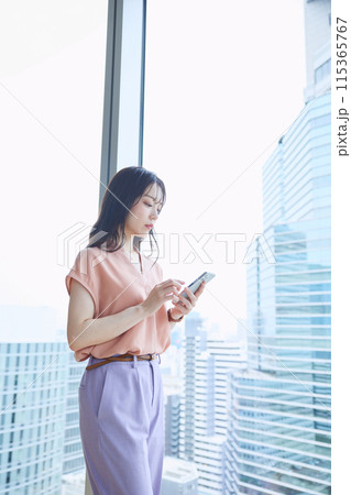 オフィスの窓辺でスマホを見る女性 オフィスの窓辺でスマホを見る女性 115365767