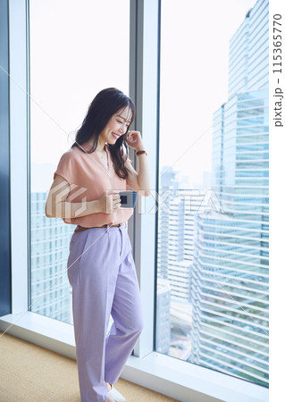 オフィスの窓辺でコーヒーを飲む女性 115365770