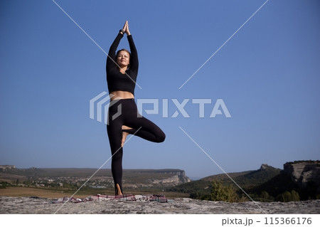 A woman is doing yoga on a rock in a beautiful mountain setting A woman is doing yoga on a rock in a beautiful mountain setting 115366176