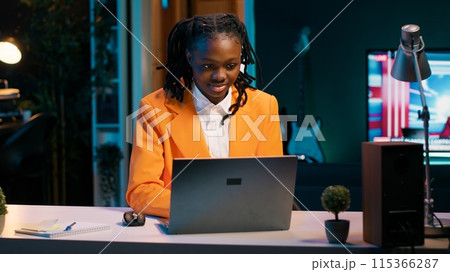 Dedicated woman diligently typing on laptop in the comfort of her home office, writing school essay to finish university homework. African american student working on improving knowledge. Camera A. 115366287