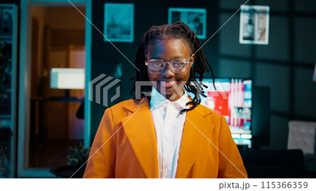 Portrait of african american student putting glasses on and working on english essays at home, reading academic databases for additional resources. Young woman studying at university. Camera B. 115366359