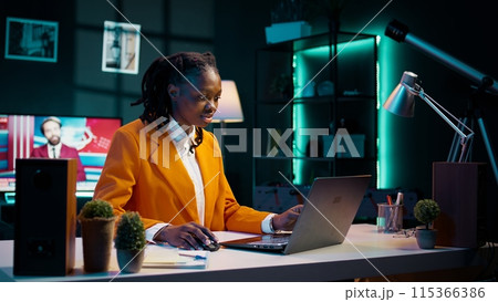 Focused student engaging in her studies at home office with laptop, determined to excel in her academics and graduate school. Hardworking girl reviews course materials and lecture notes. Camera B. 115366386