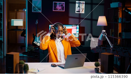 University student playing music on headphones to focus easily on college tasks and homework, writing essay for literature class. Girl enjoying modern relaxing tunes while she is working. Camera B. 115366390
