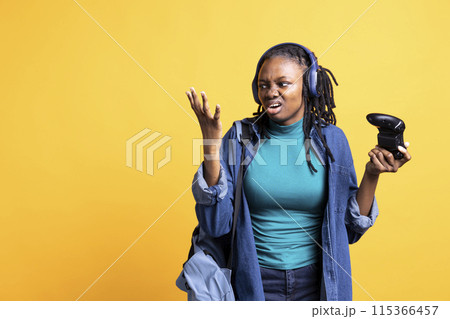 Annoyed BIPOC young girl raging after receiving game over screen, holding controller. Mad african american teenager frustrated after losing videogame, playing with gamepad, studio background Annoyed BIPOC young girl raging after receiving game over screen, holding controller. Mad african american teenager frustrated after losing videogame, playing with gamepad, studio background 115366457