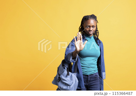 Assertive african american woman doing stop hand gesture. Annoyed BIPOC person doing firm halt sign gesturing, wishing to end concept, isolated over yellow studio background Assertive african american woman doing stop hand gesture. Annoyed BIPOC person doing firm halt sign gesturing, wishing to end concept, isolated over yellow studio background 115366487
