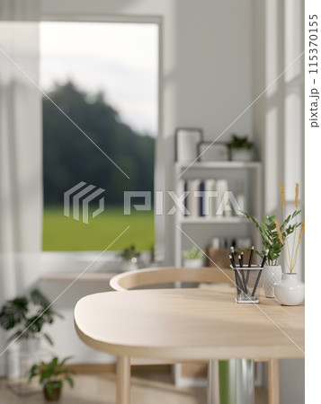 A close-up image of a wooden dining table in a small, minimalist white dining room or apartment. A close-up image of a wooden dining table in a small, minimalist white dining room or apartment. 115370155