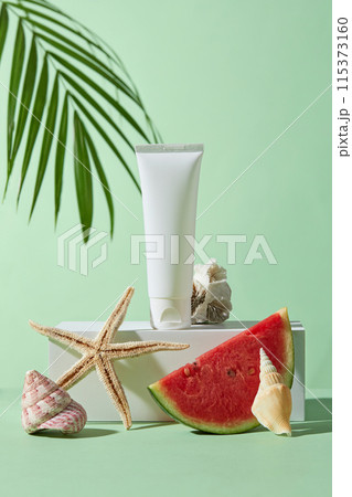 Photo of summer beach concept from front view with watermelon, coconut leaf, shell and coral decoration. Blank label cosmetic tube in white color displayed on a large podium in center, copy space Photo of summer beach concept from front view with watermelon, coconut leaf, shell and coral decoration. Blank label cosmetic tube in white color displayed on a large podium in center, copy space 115373160