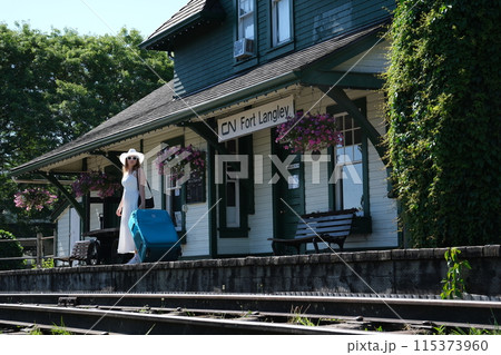 Travel alone girl with a large suitcase sits on a bench. Wait for the train white hat white dress summer 115373960