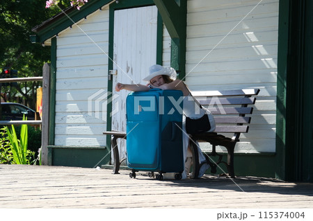 Travel alone girl with a large suitcase sits on a bench. Wait for the train white hat white dress summer 115374004