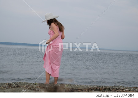 White hat Girl in a pink dress on the ocean A wide shot of a teen strolling barefoot at the beach 115374094