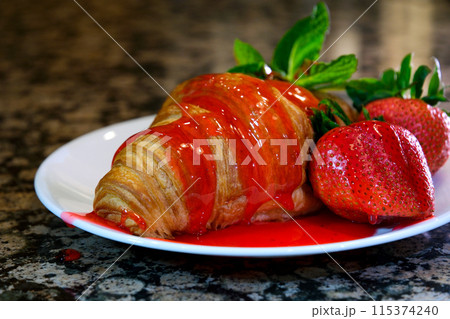 Pouring strawberry syrup on sweet croissants on white plate. Delicious croissants for breakfast or snack  115374240