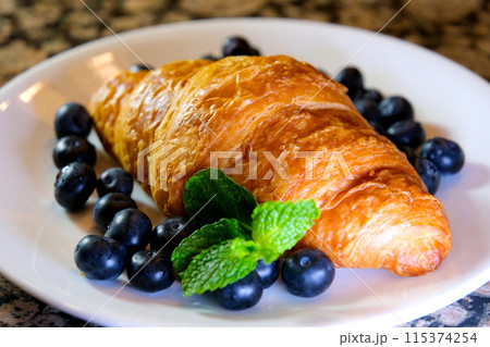 Extreme close up powdered sugar is poured onto croissants with blueberry. strainer with flour or sugar, which is sprinkled with baked goods before serving. Breakfast or dessert cooking concept 115374254
