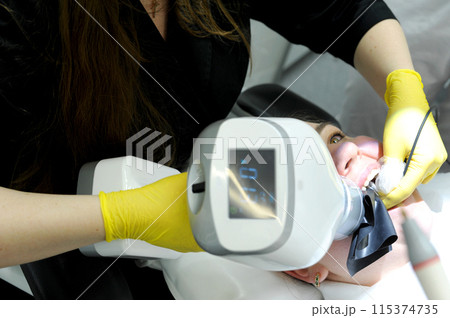 girl in an X-ray room makes a panoramic picture of her teeth. Rengen equipment in the clinic. Health care concept Patient portrait in a dental clinic girl in an X-ray room makes a panoramic picture of her teeth. Rengen equipment in the clinic. Health care concept Patient portrait in a dental clinic 115374735
