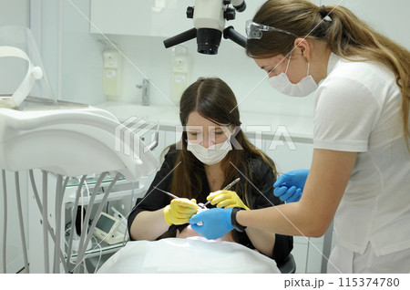Close-up medical dentist procedure of teeth cleaning the doctor and the nurse bent over the patient, they treat the teeth, they fill the canals Close-up medical dentist procedure of teeth cleaning the doctor and the nurse bent over the patient, they treat the teeth, they fill the canals 115374780