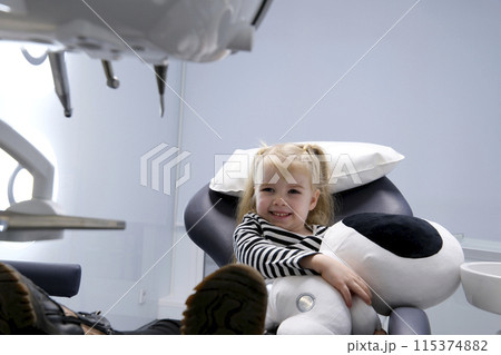 beautiful little blond blonde girl in dentist office big shoes on feet close-up latest technology soft toy in hands smile meeting the doctor alone in the frame slow slow motion camera zooms in and out 115374882