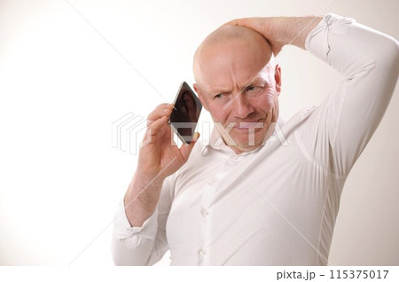 Senior man feeling upset having phone conversation depressed by hearing bad news adult man in white shirt grabbed his head and is upset, he listens to the news from the phone, he is talking to someone 115375017