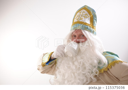 Photo of retired positive man hold mug delicious tasty beverage eggnog hot chocolate tea enjoy spending time Sinterklaas portrait. white background. Dutch Santa Claus St Nicholas christmas new year 115375036
