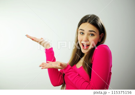 Thoughtful woman Show hands on empty space advertising looks pensively above dressed in casual pink jumper poses against blank copy space for your advertising content thinks about future 115375156