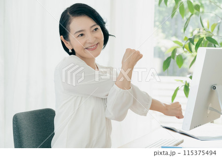 パソコンの前でストレッチをする女性 パソコンの前でストレッチをする女性 115375494