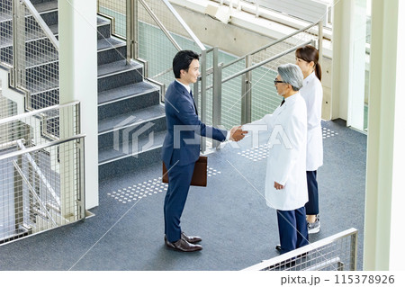 白衣の技術者と握手するビジネスマン 白衣の技術者と握手するビジネスマン 115378926