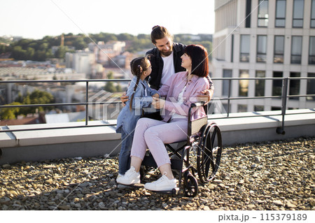 Young woman in wheelchair having fun with family on terrace of modern house. 115379189