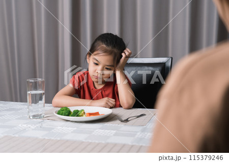 Mother is telling her cute kid eat useful vegetables but the child refuses to eat. Mother is telling her cute kid eat useful vegetables but the child refuses to eat. 115379246