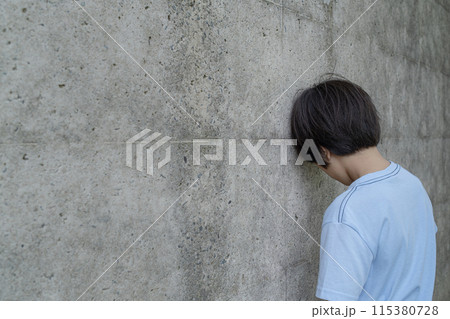 壁に寄りかかりうなだれる男の子 115380728