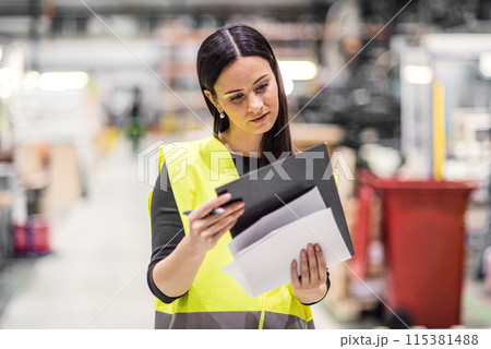 Female warehouse worker reading product order, order picking. Warehouse manager checking delivery, stock, inspecting products for the shipment. 115381488