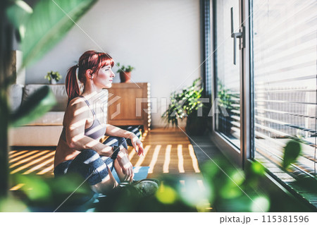 Beautiful redhead woman's home fitness routine. Home workout on gym mt in living room, sporty woman wearing sportswear. 115381596