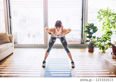 Beautiful redhead woman's home fitness routine. Home workout on gym mt in living room, sporty woman wearing sportswear. 115381613