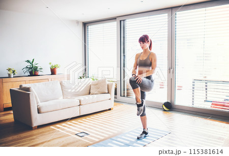 Beautiful redhead woman's home fitness routine. Home workout on gym mt in living room, sporty woman wearing sportswear. Beautiful redhead woman's home fitness routine. Home workout on gym mt in living room, sporty woman wearing sportswear. 115381614