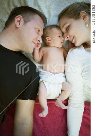 New parents lying on bed by newborn baby girl. Unconditional paternal love, idyllic family moment. New parents lying on bed by newborn baby girl. Unconditional paternal love, idyllic family moment. 115381862