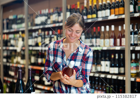 Positive woman choosing wine in supermarket Positive woman choosing wine in supermarket 115382817