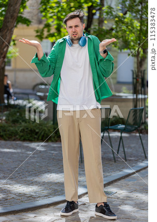 Confused young man feeling embarrassed about ambiguous question having doubts no idea outdoors Confused young man feeling embarrassed about ambiguous question having doubts no idea outdoors 115383478