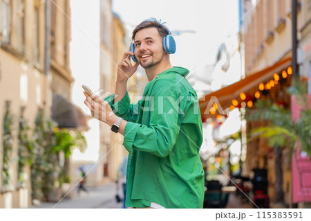 Rear view of happy relaxed man tourist in wireless headphones listening music walking on city street Rear view of happy relaxed man tourist in wireless headphones listening music walking on city street 115383591
