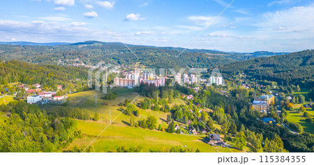 An aerial view reveals the sprawling landscape of Tanvald, stitching together dense green forests, a network of roads, and clusters of buildings under a clear sky. Jizera Mountains, Czech Republic An aerial view reveals the sprawling landscape of Tanvald, stitching together dense green forests, a network of roads, and clusters of buildings under a clear sky. Jizera Mountains, Czech Republic 115384355