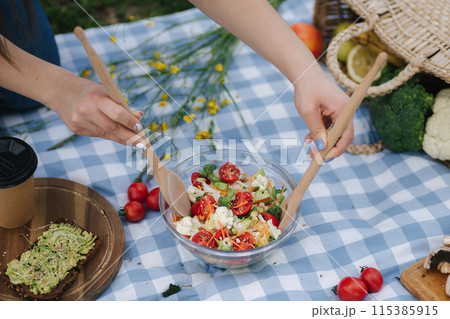 Woman mixes vegan salad on picnic outside. Vegan food concept Woman mixes vegan salad on picnic outside. Vegan food concept 115385915